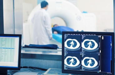 Patient lying in doughnut-shaped PET scan machine, with images of scan on computer screen.