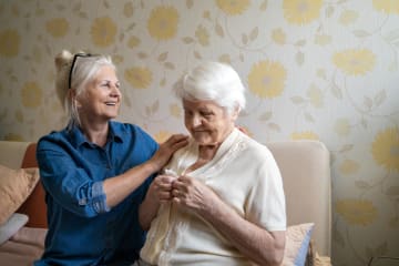 Caregiver helping senior woman dress in her bedroom