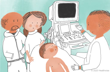 Eduardo lies on the bed while Jeff shows him the computer with wires on it