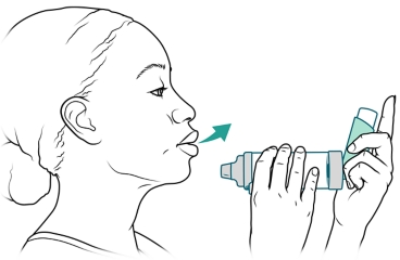 Person exhaling while holding inhaler and spacer near mouth.