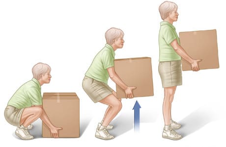 Person squatting in front of box, keeping back straight while lifting box by straightening legs, then holding box close to middle of body.